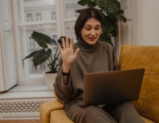 cheerful-adult-fairskinned-woman-communicates-via-video-link-with-relatives-quarantine-waving-her-hand-while-sitting-sofa-living-room-enjoying-little-things-positive-attitud en tamaño mediano